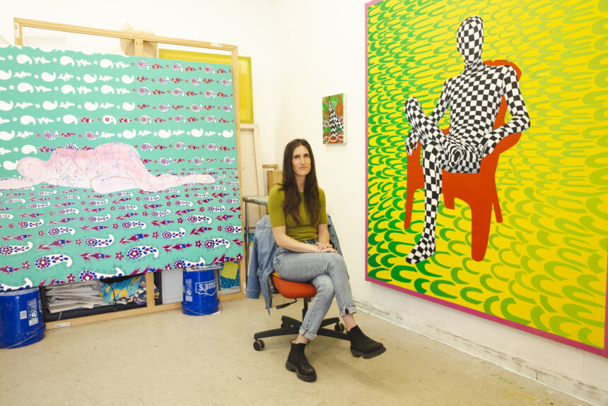 Artist, Taylor Chapin, seated in her studio next to her work, figures seated or lying down on colorful and patterned backgrounds.